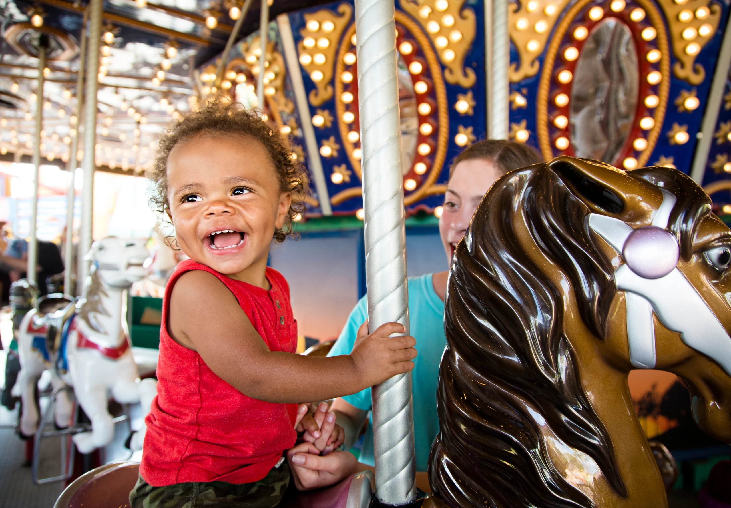 Cute Mixed Race Little Boy Enjoying A Ride On A Fun Carnival Carousel. A Happy Boy Smiling And Having Fun Riding A Carousel Ride At The Summer Carnival Laughing toddler riding a carousel horse