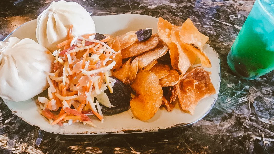 Plate of steamed bao buns, slaw, and chips with a bright green drink