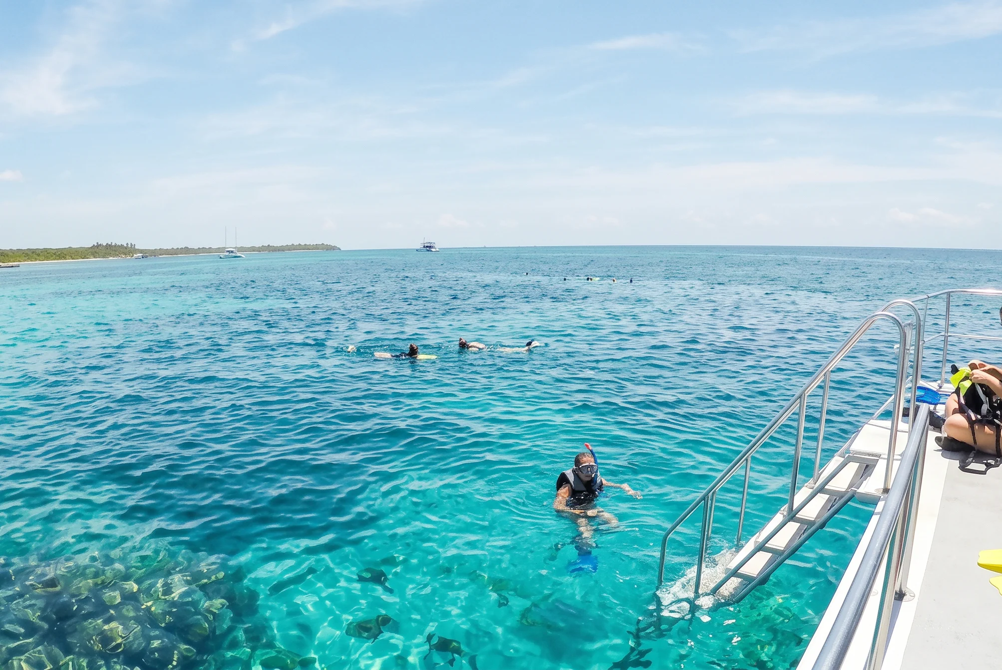 Snorkelers in clear turquoise water beside a boat's swim ladder