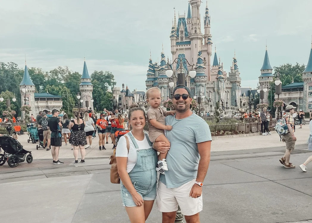 Couple holding a toddler in front of Cinderella Castle at Magic Kingdom