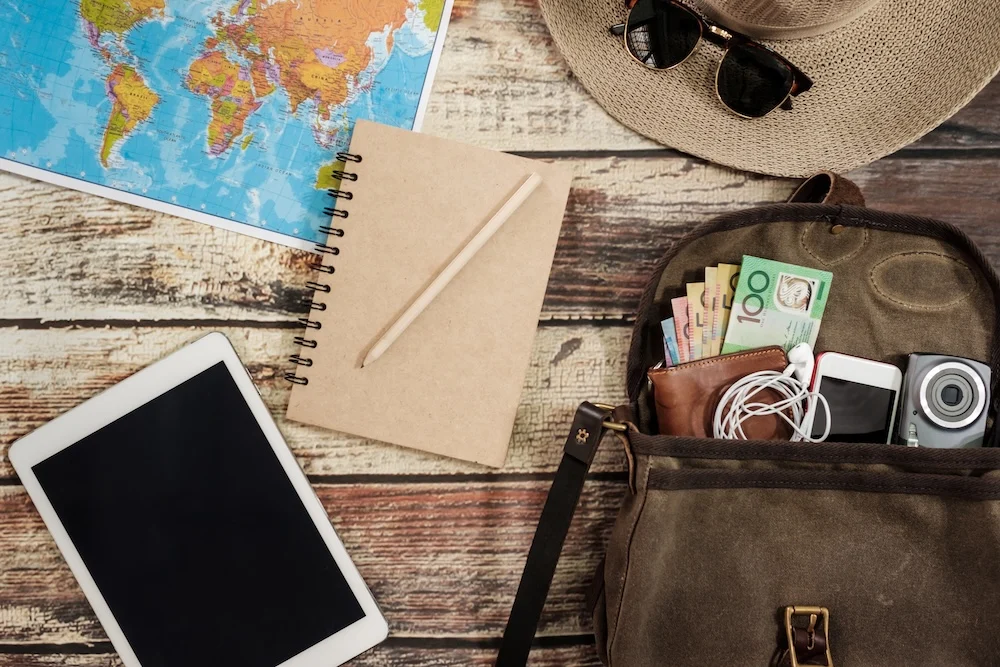 Travel planning flat lay with a map, notebook, tablet, sun hat, and camera bag